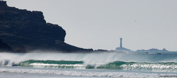 Longships beach cliffs This landscape photograph captures the dramatic Longships beach cliffs along the coast of Sennen Cove in Cornwall, United Kingdom, during a sunny afternoon in spring. The coastline is a prominent feature, with waves breaking on the beach and a rugged cliff standing to the left. In the background, the Longships Lighthouse is clearly visible on an offshore island, serving as a distinctive landmark. The image highlights the natural beauty of this part of Cornwall, where the coastal scenery and the lighthouse combine to create a well-known view of the region’s nature.